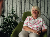 tenant smiling for photo in arm chair with hands in her lap