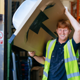 Trades operative carrying a bath tub above his head laughing 