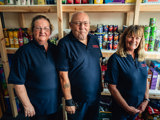 3 employees standing in front of stocked shelves at the Fylde community hub, smiling 