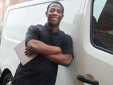 Male with arms folded holding his iPad in one hand smiling leaning against white van