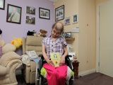 Linda smiling from her wheelchair holding a yellow book named "up the trail, fifty four years on" written by Linda herself